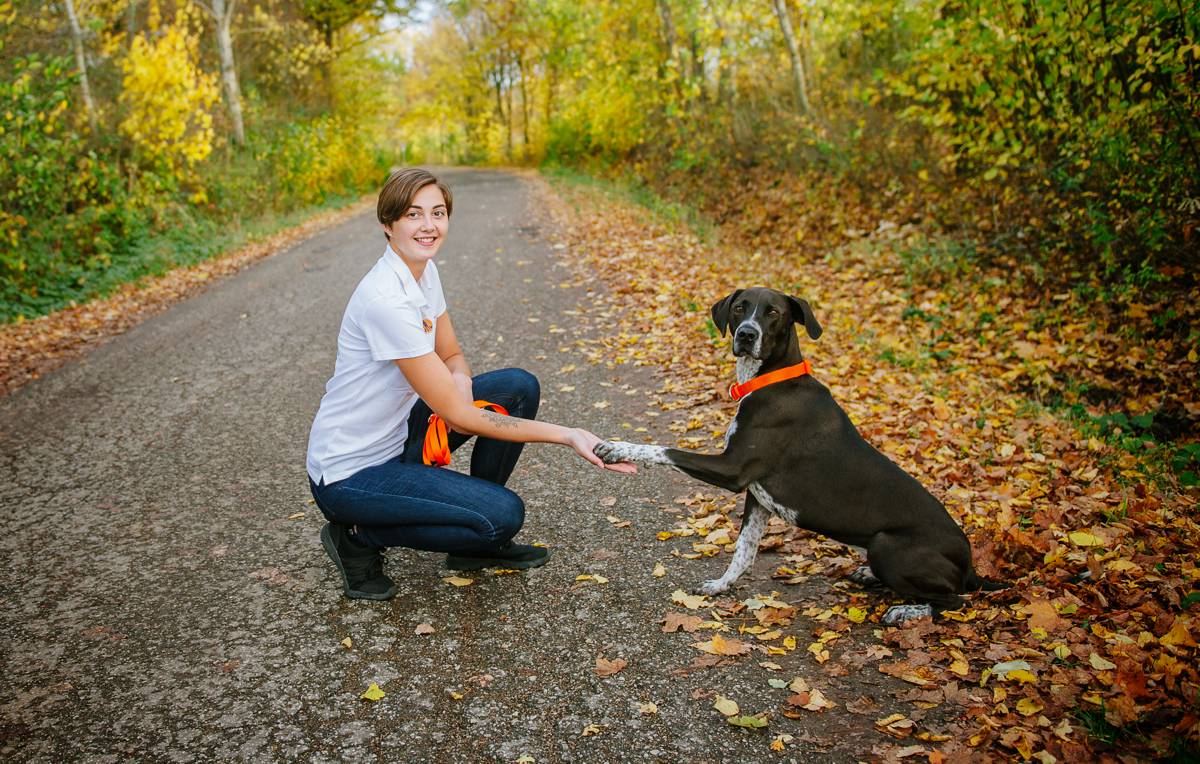 Robine Klinner beim Hundetraining vor Ort – sie gibt einem Hund auf einem herbstlichen Waldweg das Pfötchen