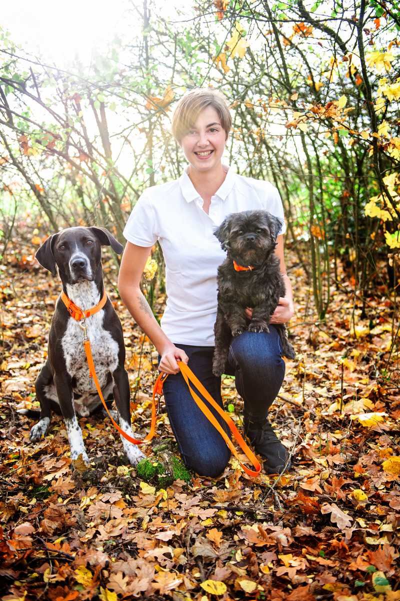 Robine Klinner hält einen Hund an der Leine auf einem herbstlichen Waldweg